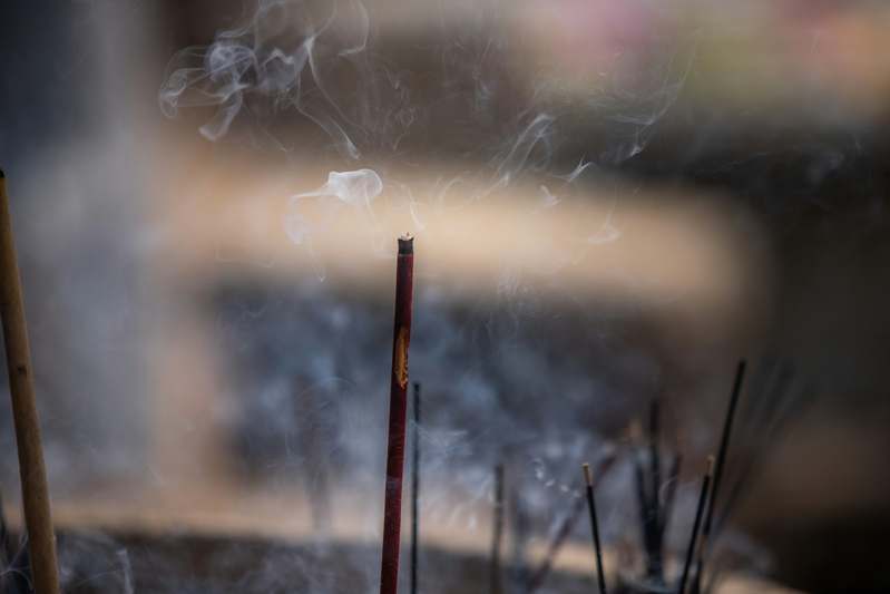 A hand holding a matte black ceramic incense burner beside dried lavender stems and a linen napkin on a warm-toned wooden table